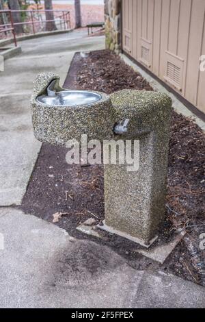 Une vieille fontaine rustique usée faite de petites pierres et galets de rivière mis en ciment toujours en usage à un parc derrière les toilettes au pique-nique Banque D'Images