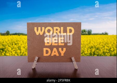 Texte de la journée mondiale des abeilles sur la carte sur la table avec un champ jaune et un fond bleu ciel. La Journée mondiale des abeilles est célébrée le 20 mai. Banque D'Images