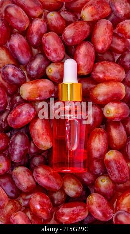 Gros plan de l'huile de pépins de raisin rose dans une bouteille, repose sur les baies de raisins rouges, frais, juteux. Banque D'Images
