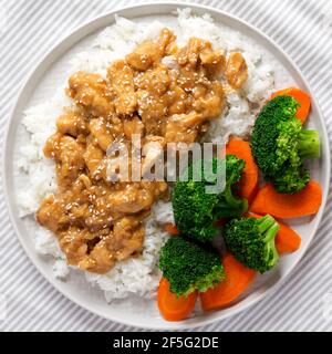 Poulet à l'orange maison avec riz blanc, brocoli et carottes sur une assiette, vue du dessus. Pose à plat, en hauteur, par le dessus. Banque D'Images