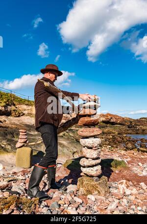 James Craig page, gerbeur en pierre, pierres empilées pour créer une sculpture sur roche sur la plage Eye Cave, Dunbar, East Lothian, Écosse, Royaume-Uni Banque D'Images