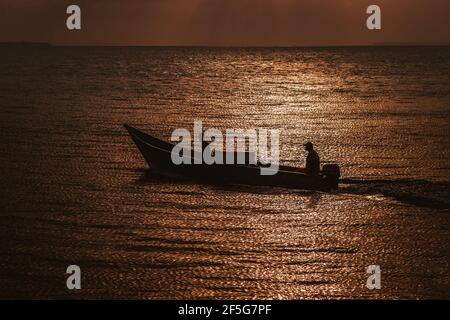 Deux pêcheurs voyagent dans un bateau au coucher du soleil dans la mer de retour à leur maison après une longue journée de travail, île Barú, Cartagena de Indias, Colombie Banque D'Images