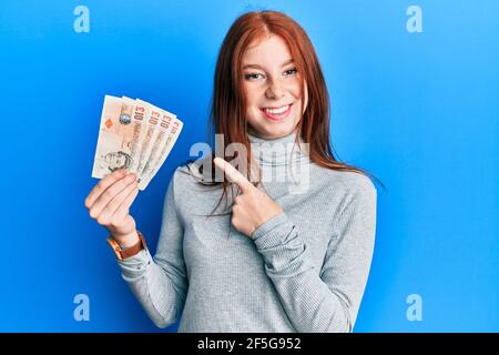 Jeune fille à tête rouge détenant 10 billets de banque au royaume-uni sourire sourire sourire sourire heureux avec la main et le doigt Banque D'Images