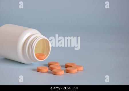 Pilules de médecine d'orange naturelle dans un pot ouvert en plastique retourné sur le devant de la table. Médecine concept des médicaments, des comprimés, des médicaments et des pilules sur fond gris. Banque D'Images