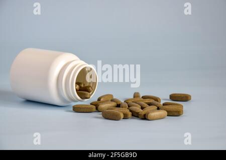 Herbe médicinale pressée brune naturelle, pilules dans un pot en plastique ouvert retourné sur le devant de la table. Médecine alternative concept de médicaments, comprimés Banque D'Images