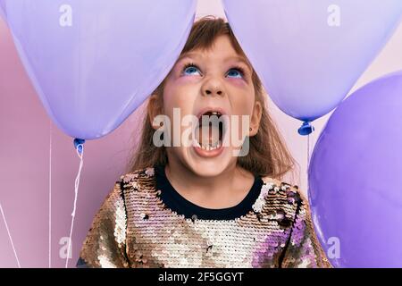 Petite fille caucasienne tenant des ballons en colère et fou criant frustré et furieux, criant avec la colère regardant vers le haut. Banque D'Images