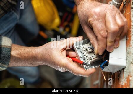 Vue de dessus. Un électricien au travail insère le câble électrique dans la pince d'un disjoncteur d'un système électrique résidentiel. Construction Banque D'Images