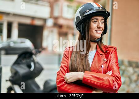 Jeune femme hispanique souriante heureuse portant un casque moto à la ville. Banque D'Images