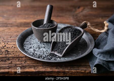 Graines de Nigella sativa également connu sous le nom de cumin noir, kalo jeera, kalonji et carvi noir dans la pelle en fer et le mortier sur fond rustique en bois Banque D'Images