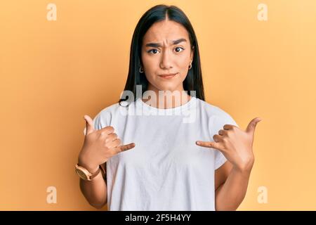 Une jeune femme asiatique faisant le signe du shaka avec les mains sceptique et nerveux, frognant contrarié à cause du problème. Personne négative. Banque D'Images