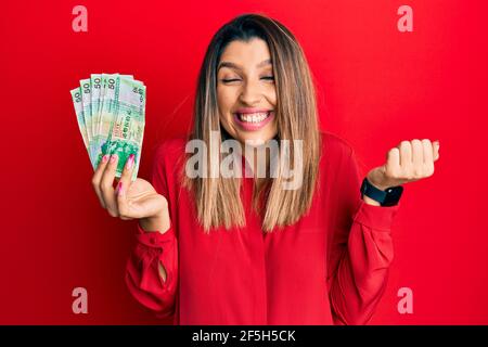 Belle femme brune tenant des billets de 50 dollars de hong kong criant fier, célébrant la victoire et le succès très excité avec le bras levé Banque D'Images