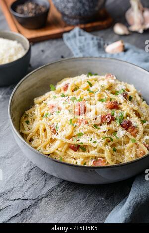 Pâtes classiques Carbonara dans une assiette en céramique, plat italien copieux à base de spaghetti, d'œufs, de bacon frit, recouvert de parmesan râpé et de pe noir Banque D'Images