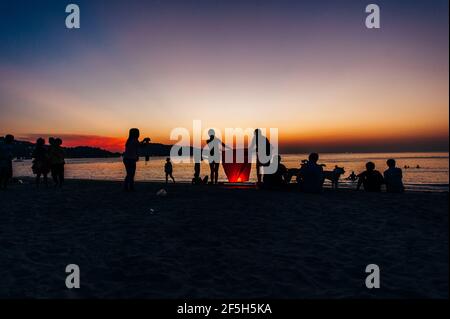 Silhouettes de personnes sur la plage. Lancement de ballons d'air chaud en papier de riz dans le ciel au coucher du soleil sur une plage en Thaïlande Banque D'Images