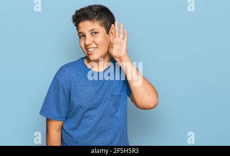 Adolescent hispanique portant des vêtements décontractés souriant de la main sur l'oreille écoutant une audition à la rumeur ou des potins. Concept de surdité. Banque D'Images