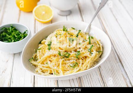 Pâtes al Limone, délicieux repas italien, spaghetti au parmesan, sauce au beurre et au citron, nappés de zeste frais râpé et de fromage sur une bosa rustique en bois Banque D'Images