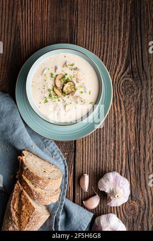 Délicieux déjeuner, soupe de champignons à la crème, accompagnée de ciboulette fraîchement hachée, servi avec du pain croustillant sur fond de bois rustique Banque D'Images