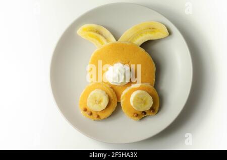 Repas créatif pour un enfant, crêpes à la banane, au chocolat et à la crème fouettée en forme de lapin, nourriture amusante Banque D'Images