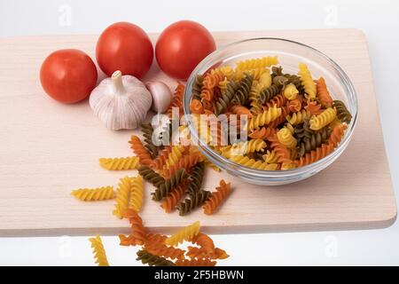 Voir à travers un bol en verre rempli de pâtes en spirale colorées non cuites sur planche à découper en bois Banque D'Images