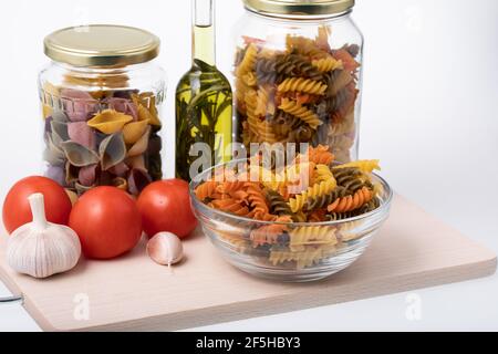 Bol en verre et bol en verre transparent plein de non cuit pâtes en spirale colorées sur planche à découper en bois Banque D'Images