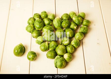 Bouquet de pousses de Brussel fraîches et brutes placées en forme de coeur sur une table en bois blanc Banque D'Images