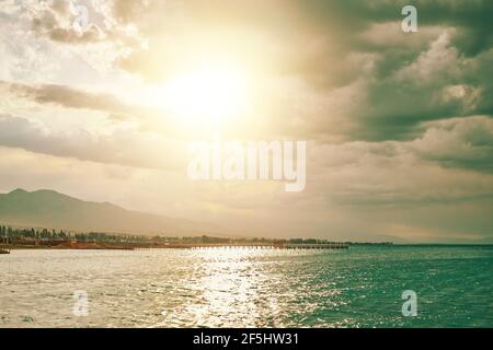 Soleil en soirée sur l'océan bleu. Superbes points d'eau. Ciel ensoleillé avec nuages en mer. Station ville et montagnes à l'horizon. Voyages, vacances d'été, tourisme. Banque D'Images