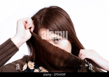 Timide jeune femme portant marron, cachant demi-visage, sur fond blanc, prise de vue en studio Banque D'Images