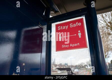 Stay Safe Stay Apart signe de distance sociale rouge avec deux caractères blancs séparés par une double flèche, sur une fenêtre d'arrêt de bus au Royaume-Uni Banque D'Images