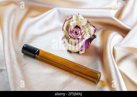 Divers contenants pour le stockage de cosmétiques en verre foncé se trouvent sur les plis de tissu satiné de soie, entouré de fleurs de rose séchées. Parfum, sérum ou Banque D'Images