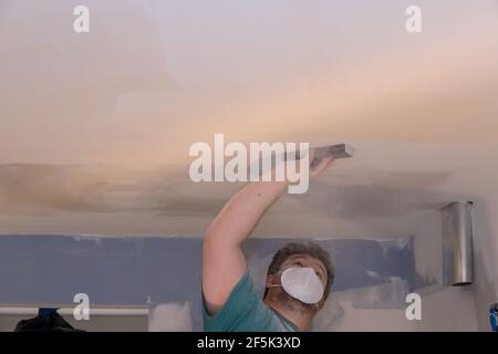 Entrepreneur utilisant une truelle de sable ponçant la cloison sèche de placoplâtre plafond pendant la rénovation de la chambre Banque D'Images