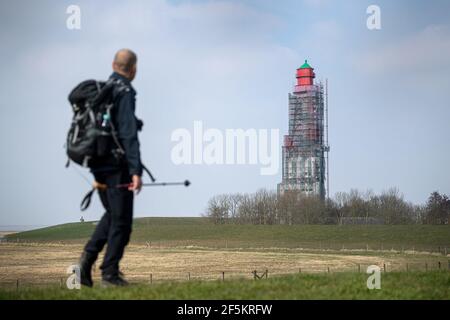 24 mars 2021, Basse-Saxe, Krumhörn : un marcheur passe devant le phare de Campen, doté d'un échafaudage. Le phare le plus haut d'Allemagne est en cours de rénovation. Photo: Sina Schuldt/dpa Banque D'Images