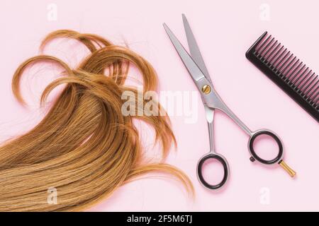 Ciseaux, un peigne et un fil coupé de cheveux blonds femelles pour enfants sur fond rose, vue du dessus. Concept de coiffure. Banque D'Images