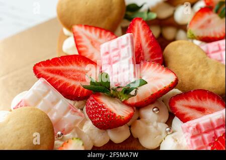Génoise aux fraises, barres de chocolat au lait rose, asperges argentées, crème à la vanille et petits gâteaux à la cape en forme de coeur. Dessert sucré d'été pour bi Banque D'Images