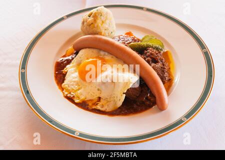 Fiakergulasch ou Herrawlasch Goulash viennois au bœuf, garni d'un boulonnage de pain, de saucisses de Francfort, d'œufs frits et de gherkine sur une assiette Banque D'Images