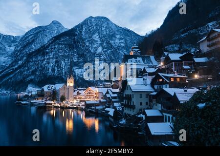 Hallstatt CityScape lors d'une soirée d'hiver froide couverte de neige Avec le lac Hallstaetter Voir et l'église illuminée la nuit Banque D'Images