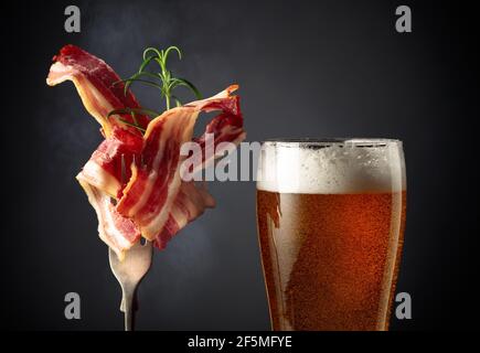 Verre de bière et tranches de bacon frit garni de romarin. Banque D'Images