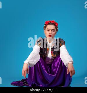 Une jeune femme en tenue ethnique, de style espagnol ou mexicain, un mélange de cultures et de styles. Portrait sur fond bleu dans le studio. Banque D'Images
