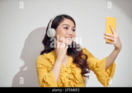 Portrait de jeune fille gaie en casque blanc fait selfie sur smartphone isolé sur fond blanc Banque D'Images