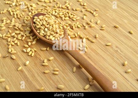 Beaucoup de grain de blé sec dans une cuillère en bois, sur la planche à découper en bambou Banque D'Images