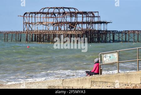 Brighton Royaume-Uni 27 mars 2021 - détente au bord de la jetée ouest sur un matin lumineux et ensoleillé mais frais sur le front de mer de Brighton . Le temps devrait devenir beaucoup plus chaud la semaine prochaine avec des températures qui devraient atteindre plus de 20 degrés dans certaines parties du Royaume-Uni : crédit Simon Dack / Alamy Live News Banque D'Images