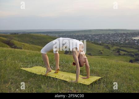 FIT femme mature pratiquant Urdhva Dhanurasana sur une colline verte tranquille en campagne Banque D'Images