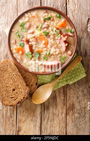 Soupe d'orge et de haricots Richet avec viande fumée et légumes en gros plan dans un bol sur la table. Vue verticale du dessus Banque D'Images