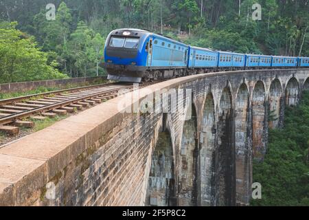 Un train bleu traverse le viaduc du pont Demodara Nine Arches en passant par le pays de la colline de la jungle du Sri Lanka lors d'un voyage pittoresque. Banque D'Images