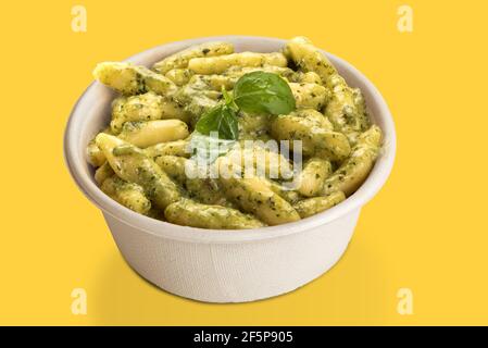 Gnocchi avec sauce pesto génoise dans une plaque de carton à emporter, isolée sur fond jaune Banque D'Images