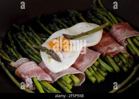 Asperges enrobées de bacon avec un œuf frit sur le dessus Banque D'Images
