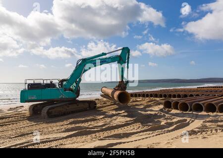 Pelle hydraulique Ovenden SK500 déplaçant de gros tuyaux avec de gros tuyaux sur la plage pour des travaux de réapprovisionnement de plage à Bournemouth et Poole Beaches, Dorset, Royaume-Uni Banque D'Images