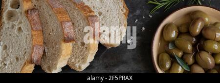 Pain de ciabatta en tranches italiennes sur planche à découper avec herbes, huile extra vierge et olives marinées sur fond de grunge foncé Banque D'Images