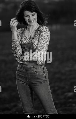 Portrait extérieur d'une jeune femme souriante et vêtue salopette dans la campagne en noir et blanc Banque D'Images