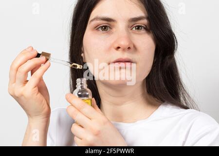 Femme tenant de l'huile écologique naturelle pour le visage dans une bouteille en verre avec une pipette. Cosmétologie et soins du visage et du cou Banque D'Images