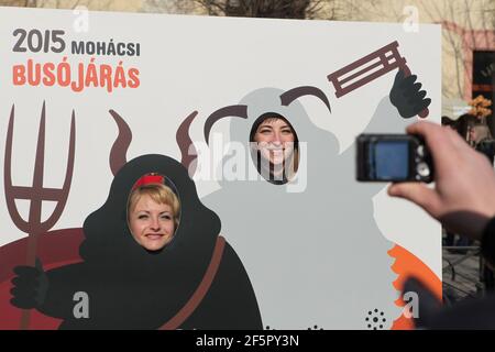 Les gens prennent des photos comme les Busós en utilisant un stand-in de photo pendant le carnaval de Busójárás à Mohács dans le comté de Baranya, Hongrie. Célébration traditionnelle annuelle masquée du groupe ethnique Šokci tenue à la fin de la saison du carnaval (Farsang) dans le sud de la Hongrie. Banque D'Images