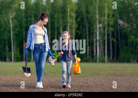 La mère heureuse et la petite fille gamin vont ensemble planter un plantule d'arbre vert. Les parents apprennent à l'enfant à propos de l'environnement et de l'éco-soin de la nature. FAM Banque D'Images